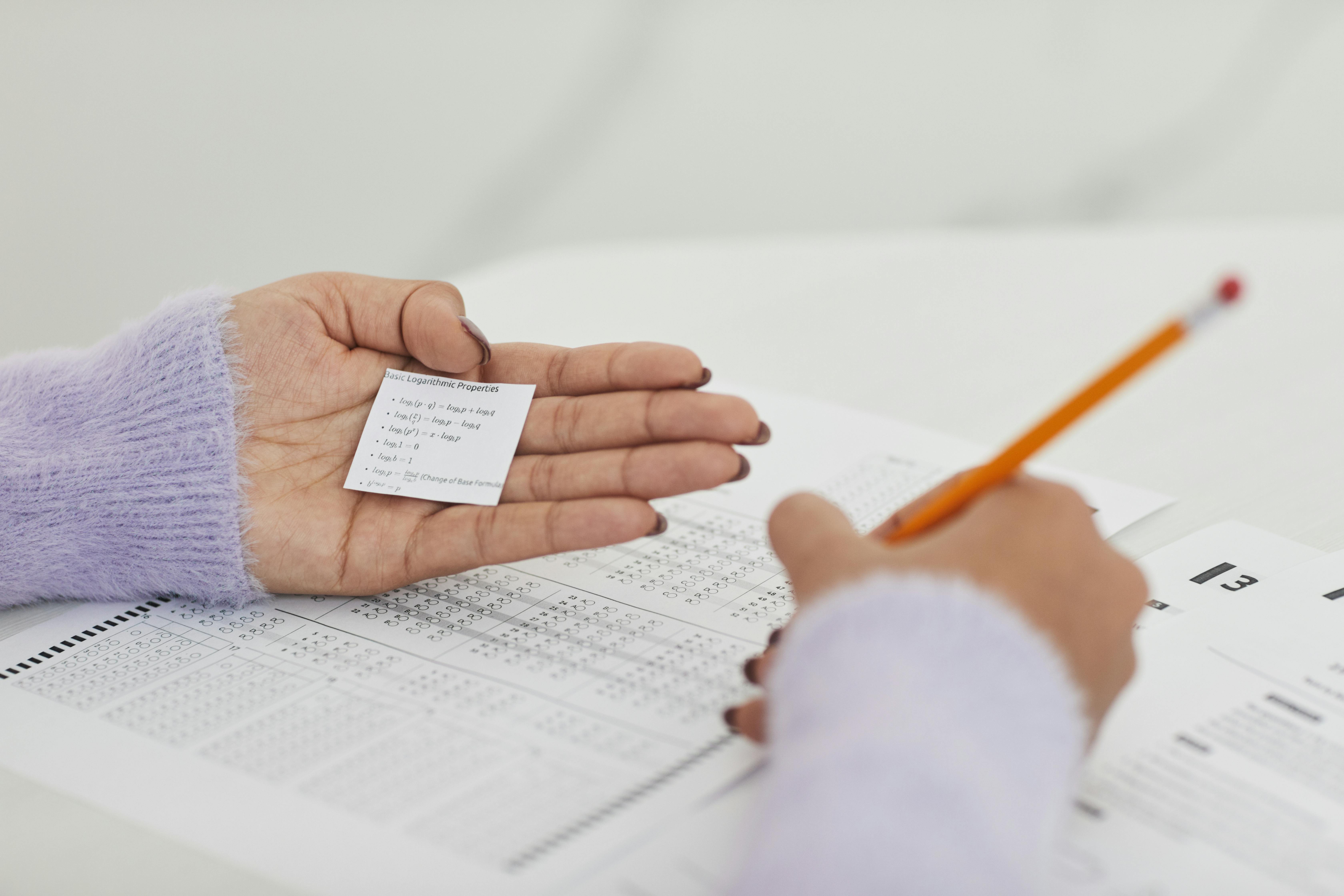 A student copying the answers to a test from a piece of paper in their hand.